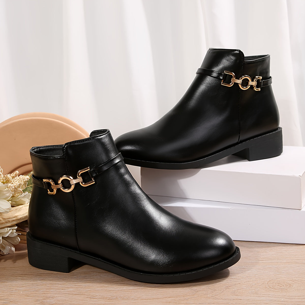 Briar gold chain ankle boots in black leather, pair on a white display block