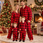Family wearing matching red plaid Christmas pajamas by the tree