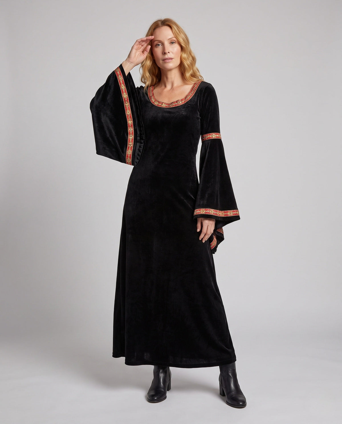 Woman wearing a black velvet hooded costume dress with bell sleeves and red and gold trim