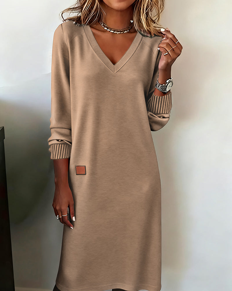 Woman wearing a relaxed V-neck midi sweater dress with raglan long sleeves and striped cuffs