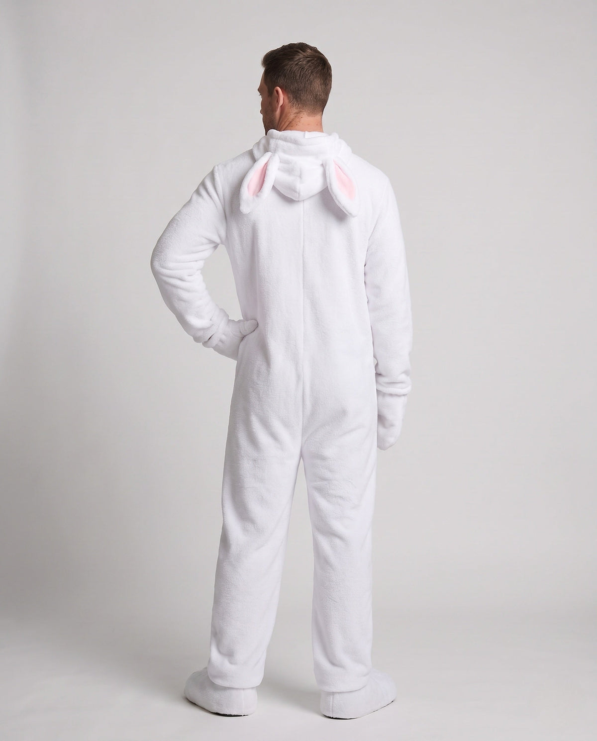 Man wearing a white plush bunny costume jumpsuit with pink belly panel and eared hood - view 3