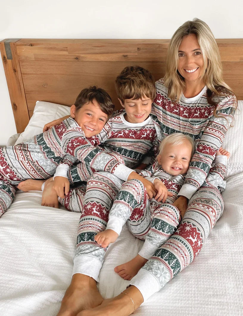 Family wearing matching gray Fair Isle Christmas pajamas with red reindeer and green tree stripes