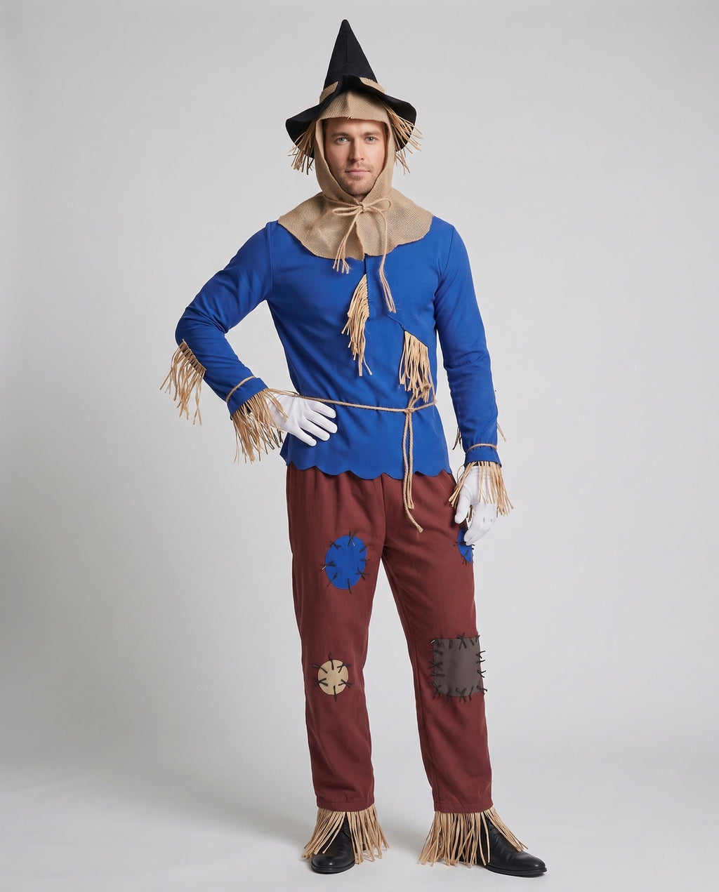 Men's scarecrow Halloween costume with blue fringed top, burlap-look hood, patched red pants, black hat and white gloves