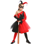 Girl wearing a red and black jester Halloween costume with one-shoulder bodice, pom-pom trim, tulle skirt and black eye mask - view 3